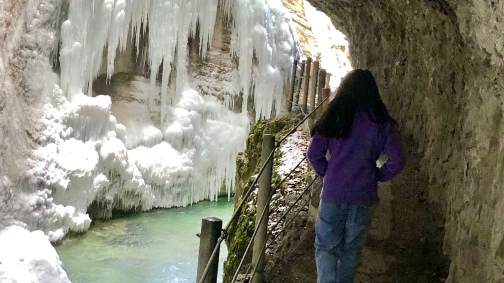 A girl hiking along the icy blue river with icicles formed on the rock formations along the partnach gorge in germany