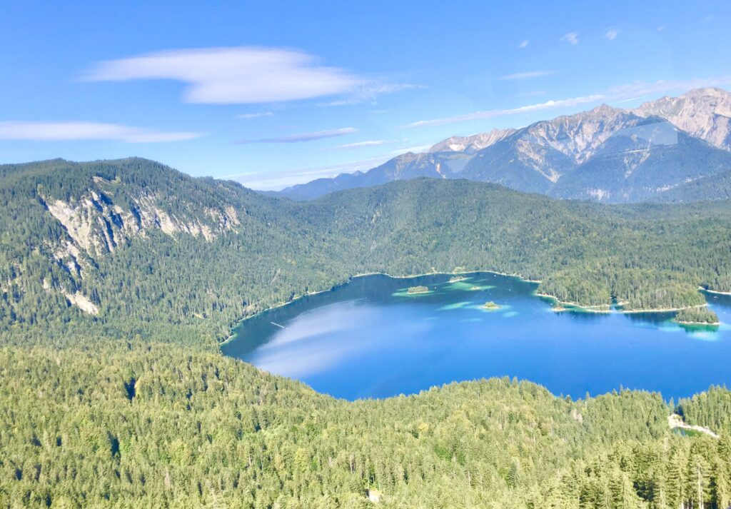 A view from the top of the Zugspitze mountain in Germany looking towards a beautiful mountain lake and its surrounding mountain peaks on a sunny day. 